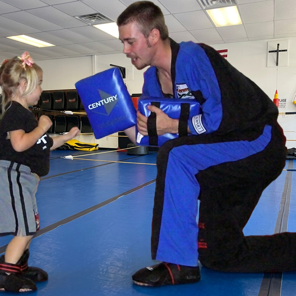 A preschooler punching a pad held by her kneeling instructor in a Super T Tigers class in Grand Rapids